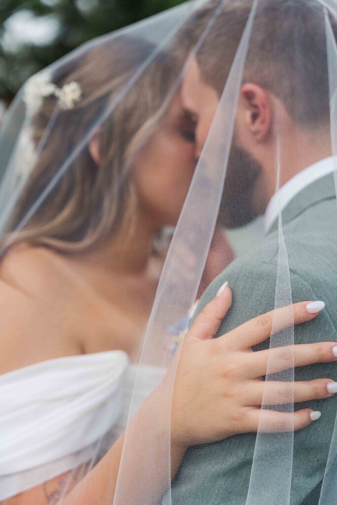 bride and groom cuddling just married with veil over them 